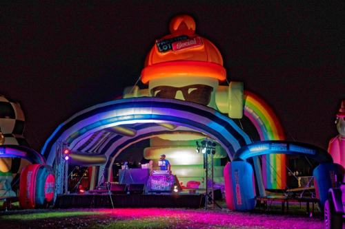 A colorful inflatable stage with a DJ under a large, illuminated character at night.