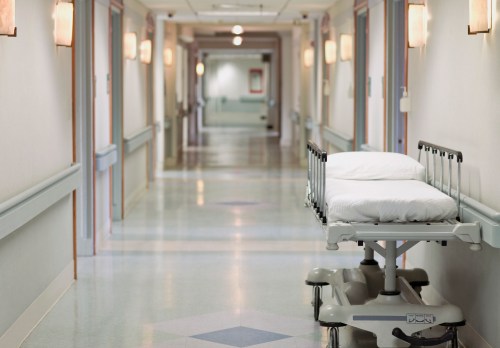 A hospital corridor with a vacant stretcher on wheels and soft lighting along the walls.