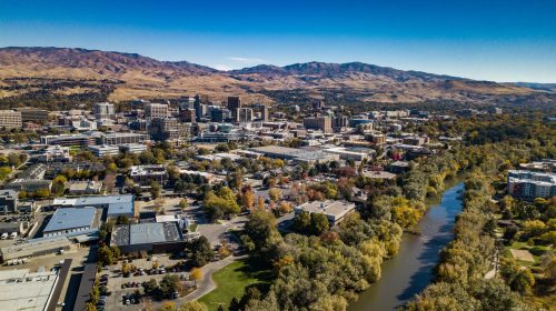 Aerial view of a city with mountains in the background, featuring buildings, trees, and a river running through.