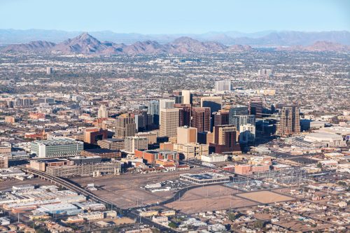 Aerial view of a city skyline with mountains in the background and urban development in the foreground.
