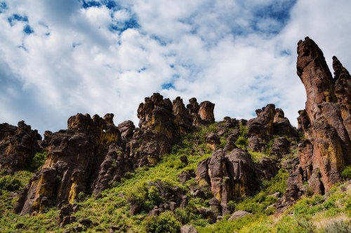 A rugged landscape featuring towering rock formations against a cloudy sky, surrounded by lush greenery.