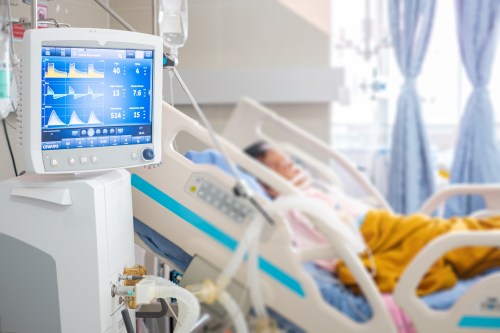A hospital room with a patient in bed and a monitor displaying vital signs in the foreground.