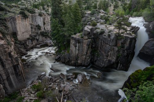 A scenic view of a waterfall cascading over rocky cliffs, surrounded by lush greenery and flowing river below.