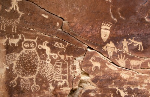Petroglyphs depicting animals and human figures carved into a rocky surface, showcasing ancient artistry.