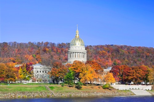 West Virginia State Capitol surrounded by vibrant autumn foliage and a clear blue sky.