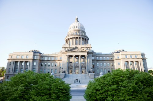 The Idaho State Capitol building with a large dome, surrounded by greenery and a clear blue sky.