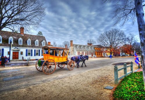 A horse-drawn carriage on a historic street lined with colonial-style buildings and bare trees under a cloudy sky.