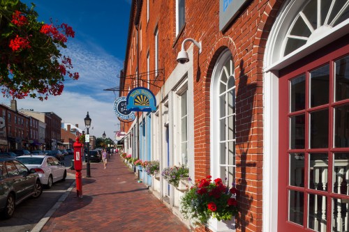 A charming brick street lined with shops, colorful flower boxes, and a clear blue sky.