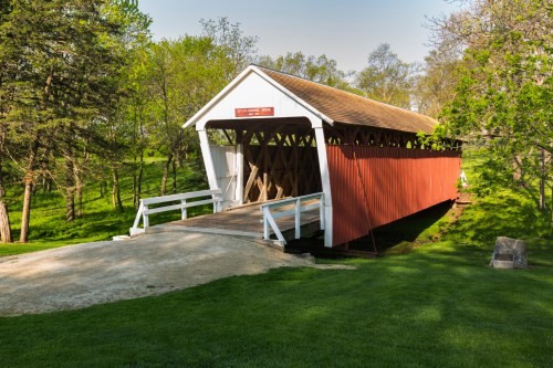 A red and white covered bridge surrounded by green trees and grass on a sunny day.