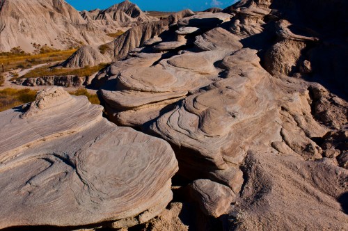 A rocky landscape with smooth, wavy formations under a clear blue sky, showcasing natural erosion patterns.