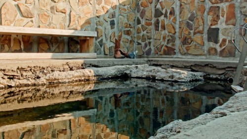 A tranquil scene featuring a stone wall beside a still water pool, reflecting the surroundings.