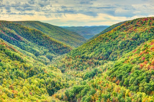 A panoramic view of lush green valleys with autumn foliage, under a cloudy sky.