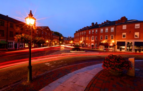 A charming street scene at dusk, featuring brick buildings, a lamppost, and light trails from passing cars.