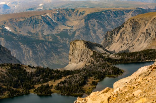 A panoramic view of rugged mountains and a winding river, surrounded by lush greenery and rocky terrain.