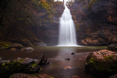 A serene waterfall cascades into a tranquil pool, surrounded by moss-covered rocks and lush greenery.