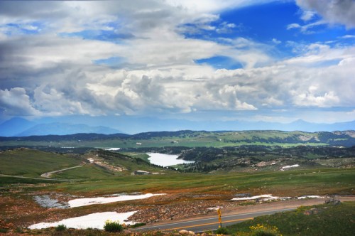 A scenic landscape featuring rolling green hills, a lake, and a dramatic sky with clouds.