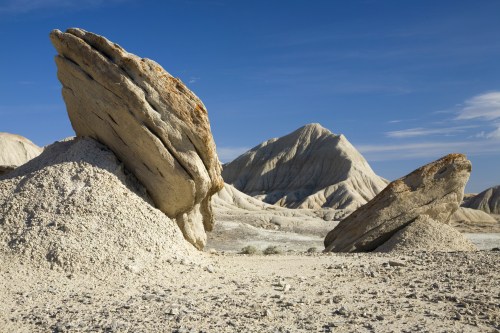 A barren landscape featuring large, weathered rock formations and a distant mountain under a clear blue sky.