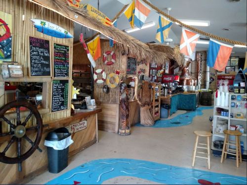 A colorful beach-themed shop interior with tiki decor, flags, and a menu board, featuring a tropical vibe.