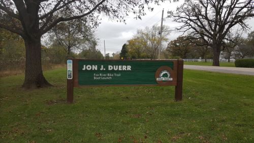 Sign for Jon J. Duerr Boat Launch, featuring the Fox River Bike Trail, surrounded by grass and trees.