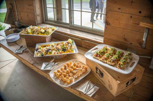 A rustic table displays an assortment of colorful dishes, including salads, appetizers, and seafood, near a window.