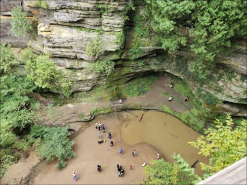 Aerial view of a rocky canyon with a small group of people gathered around a muddy area surrounded by greenery.
