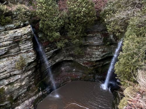 A serene waterfall cascades into a rocky gorge, surrounded by lush greenery and moss-covered cliffs.