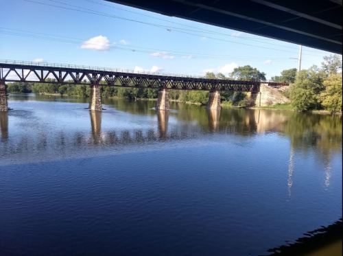 A tranquil river scene featuring a railway bridge reflecting in the water under a clear blue sky.