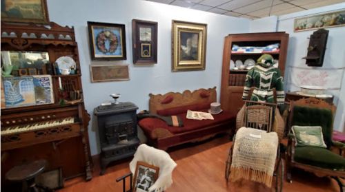 A cozy vintage room featuring antique furniture, a small stove, and various framed artworks and decor items.