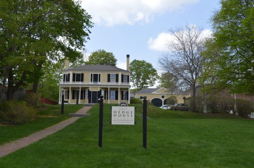 A yellow house with a circular design, surrounded by greenery, featuring a sign that reads "Hedge House."