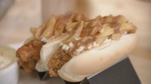 Two hot dogs topped with crispy fries and gravy, served on a wooden table.