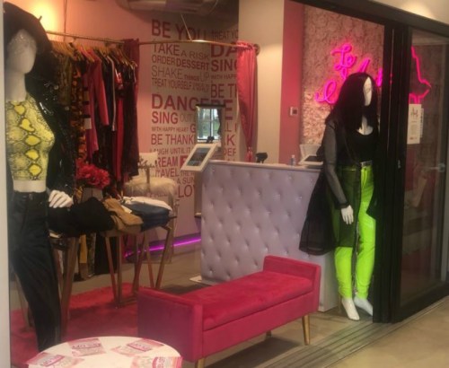 A boutique display featuring stylish mannequins, vibrant clothing, and a pink seating area.