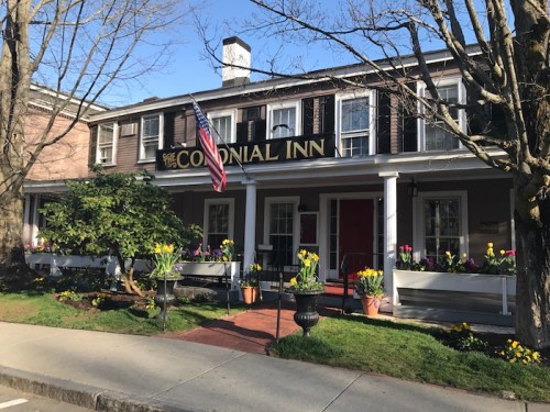 Front view of the Colonial Inn, featuring an American flag and colorful flower pots along the porch.