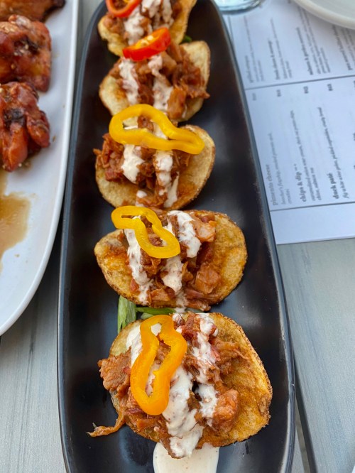 A platter of crispy potato chips topped with pulled chicken, drizzled with sauce, and garnished with yellow peppers.