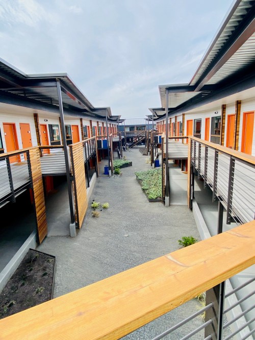 A view of a modern courtyard with orange doors and wooden walkways connecting two rows of buildings.