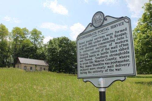 Historical marker about Confederate postal services, with a rustic building and grassy field in the background.