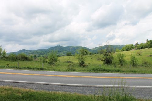 A scenic view of rolling green hills under a cloudy sky, with a road in the foreground.
