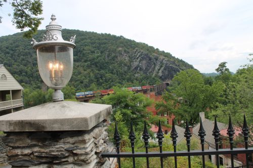 A vintage lamp post in the foreground with a scenic view of mountains and a train passing through lush greenery.