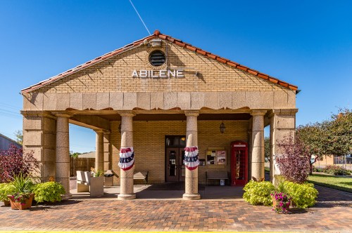 Historic building with "Abilene" sign, columns, and decorative plants under a clear blue sky.