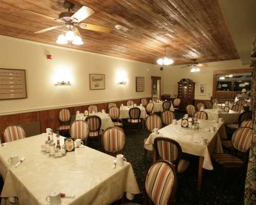 A cozy restaurant interior with striped chairs, tables set for dining, and warm lighting.