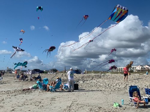 Colorful kites flying over a beach with people relaxing on chairs and enjoying the sunny day.