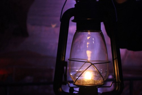 A close-up of a vintage lantern glowing softly in a dimly lit cave setting.