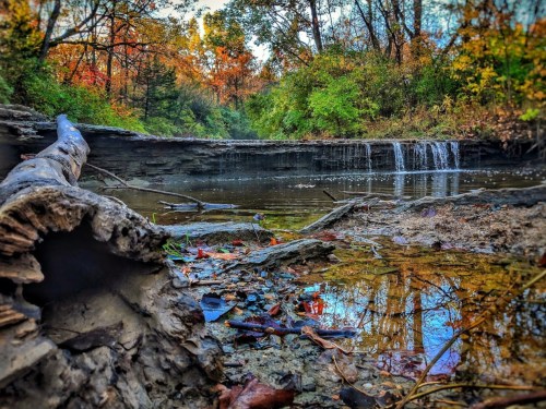 A serene landscape featuring a small waterfall, surrounded by colorful autumn foliage and a rocky shoreline.