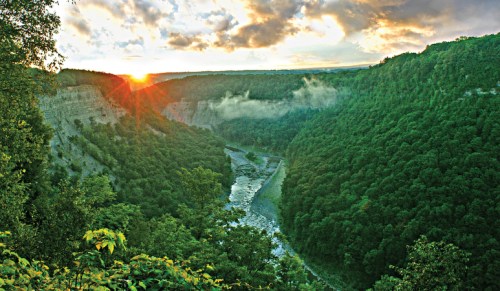 A scenic view of a river winding through a lush green valley at sunset, with mist rising from the trees.