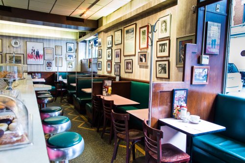 A cozy diner interior with green booths, a counter, and walls adorned with framed photos and memorabilia.