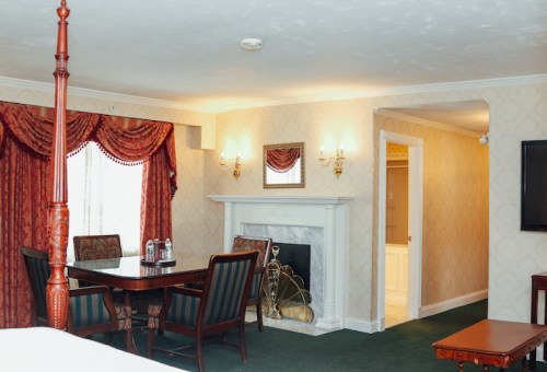 A cozy hotel room featuring a dining area, fireplace, and elegant decor with patterned wallpaper and rich curtains.