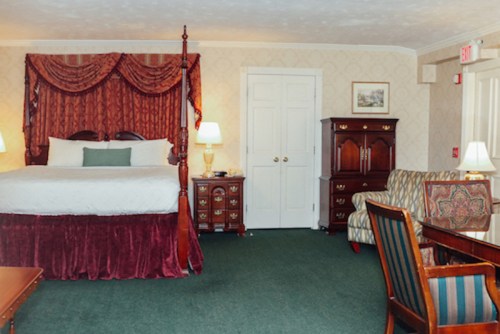 Cozy hotel room featuring a four-poster bed, elegant decor, a seating area, and wooden furniture.