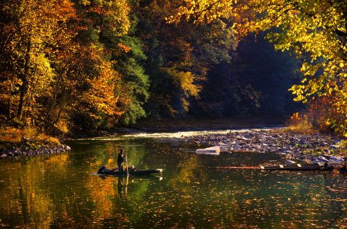 A person paddles a canoe on a serene river surrounded by vibrant autumn foliage and calm waters.
