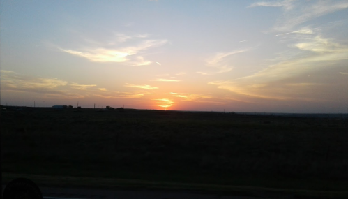 A serene sunset over a vast, open landscape with soft clouds and a warm glow on the horizon.