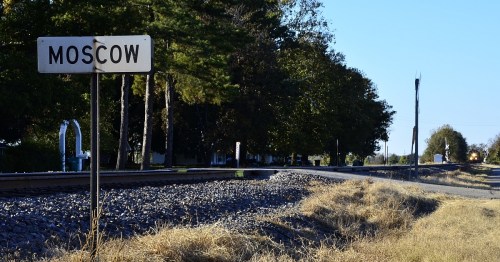 Sign for Moscow next to a railway track, with trees and a clear blue sky in the background.