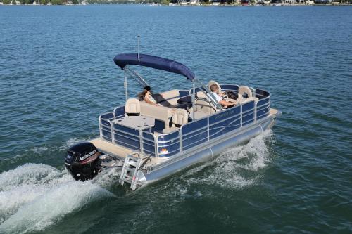 A blue pontoon boat with passengers cruising on a calm lake, leaving a wake behind.
